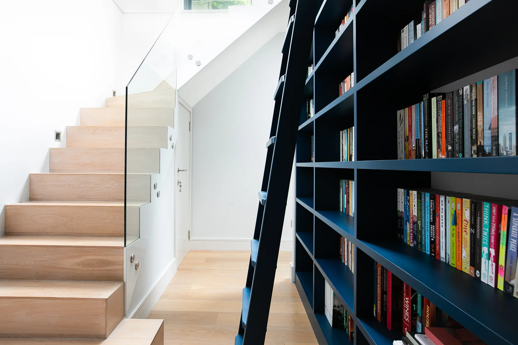 Bespoke blue library shelving alongside a light-filled staircase in Wandsworth